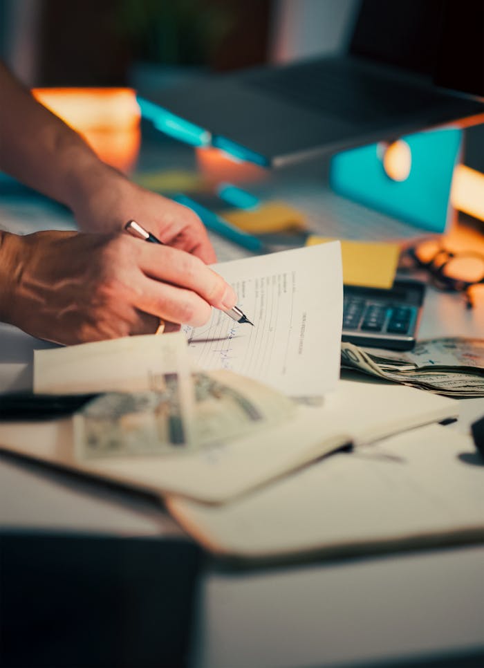 services-03 A hand signing financial documents on a desk with cash and a calculator, signifying finance management.